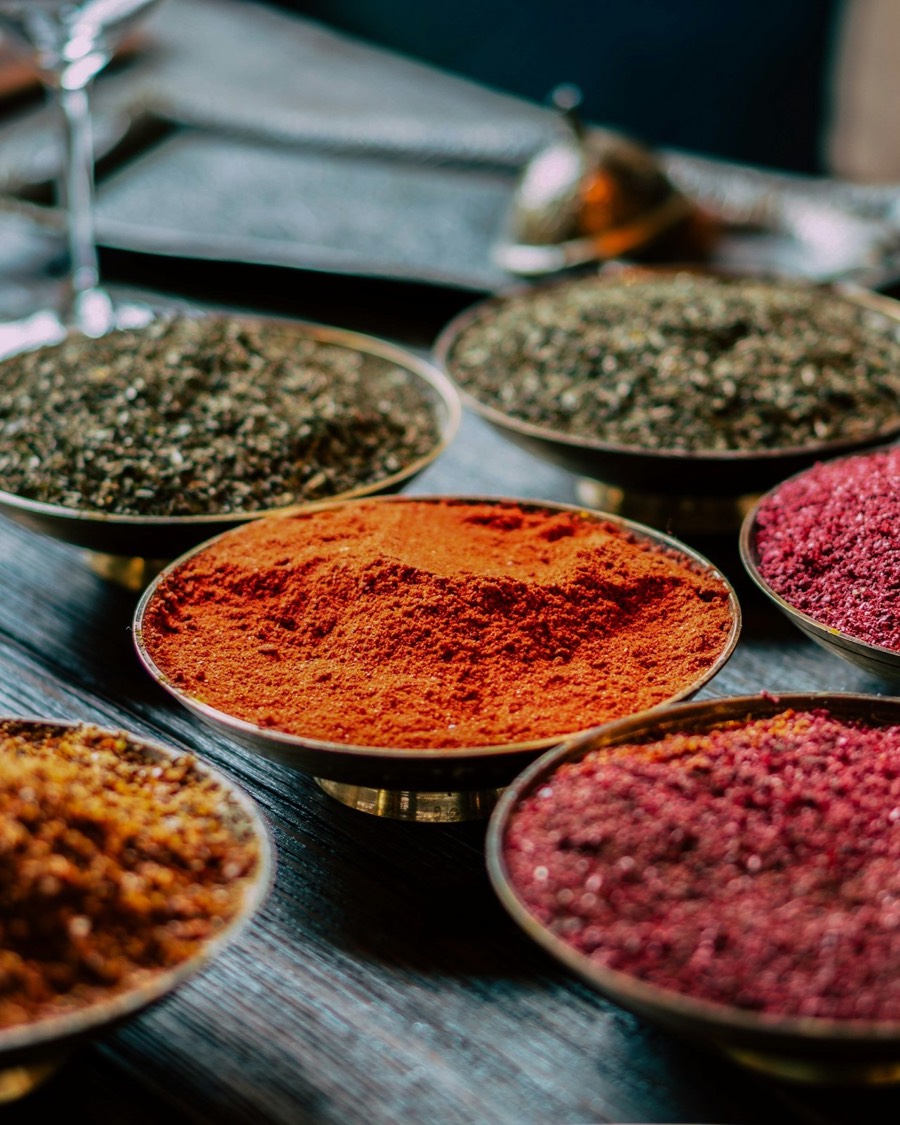 Brass bowls heaped with ground spices — paprika, sumac and dried herbs — on a dark wooden table